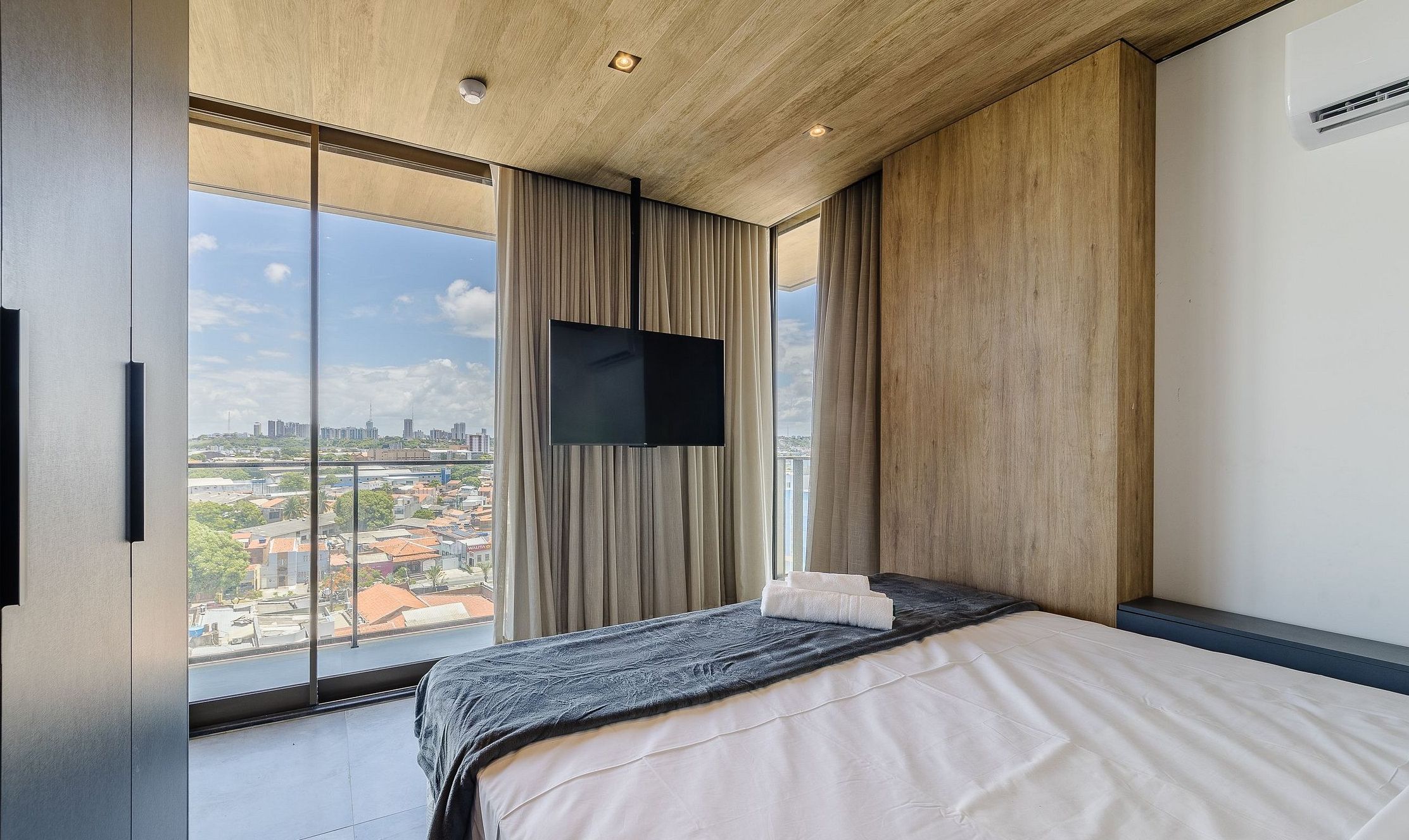 A modern hotel room with a large bed, a flat-screen TV, and a city view.