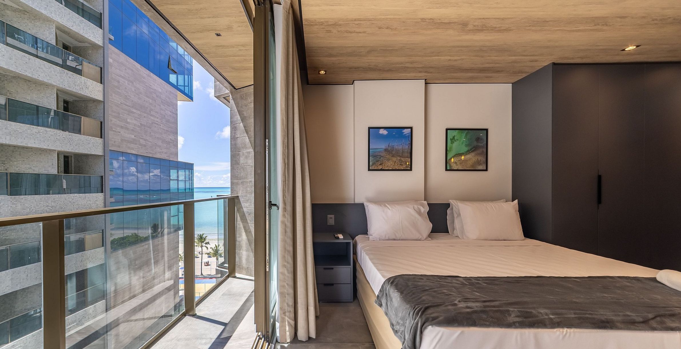 A modern hotel room with a balcony, a bed, two bedside tables, and artwork on the walls.