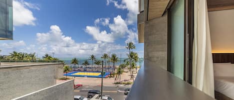 Un balcón de hotel con vista a una playa, palmeras y una cancha de baloncesto.