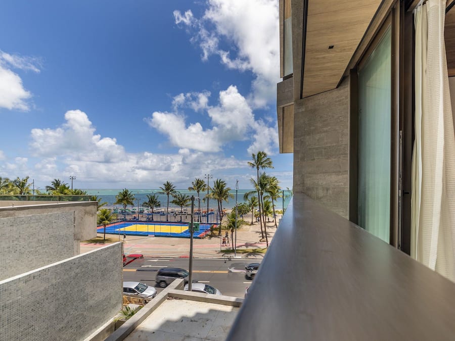 Un balcón de hotel con vista a una playa, palmeras y una cancha de baloncesto.