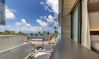 A hotel balcony with a view of a beach, palm trees, and a basketball court.