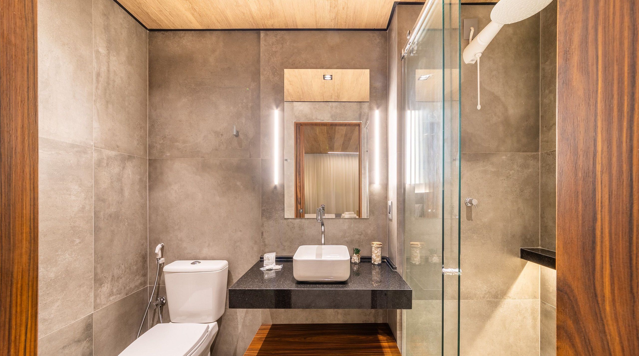 A modern bathroom with a glass shower enclosure, a white toilet, and a black countertop with a sink.