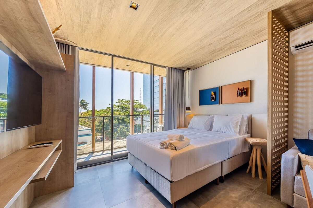 Ein modernes Hotelzimmer mit einem großen Bett, einem Fernseher, einem Balkon mit Blick auf die Stadt und einer Holzbalkendecke.
