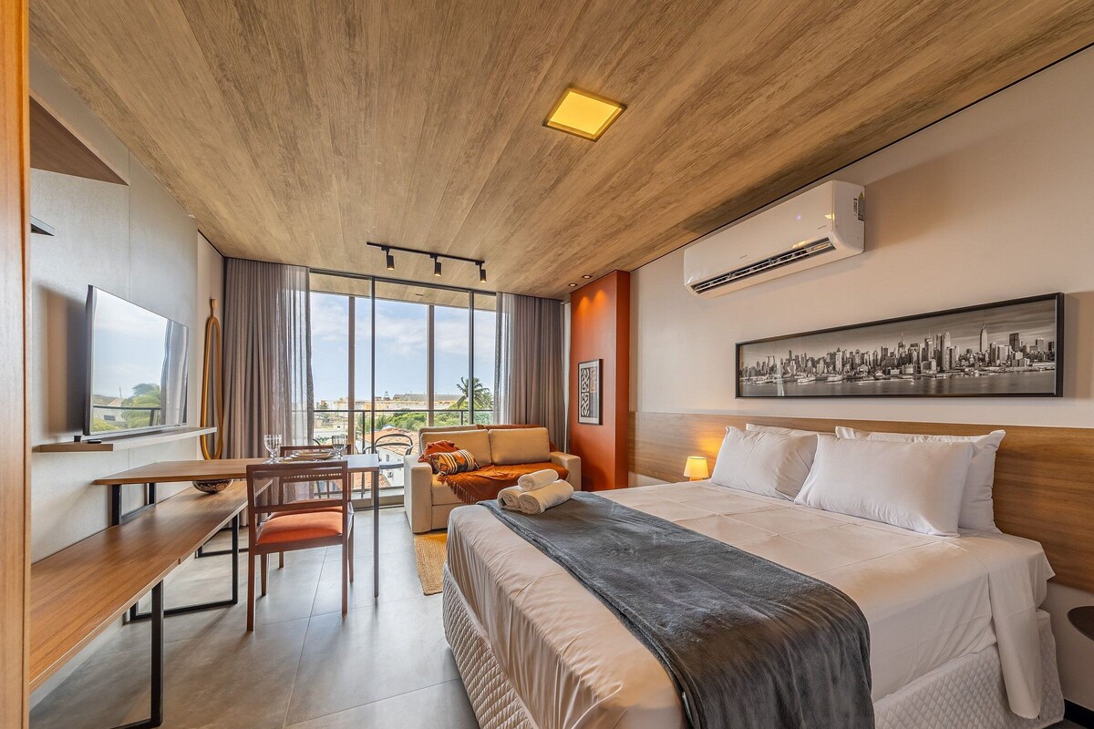 Ein Hotelzimmer mit Bett, Schreibtisch, Stuhl, Sofa und großem Fenster mit Blick auf die Stadt.