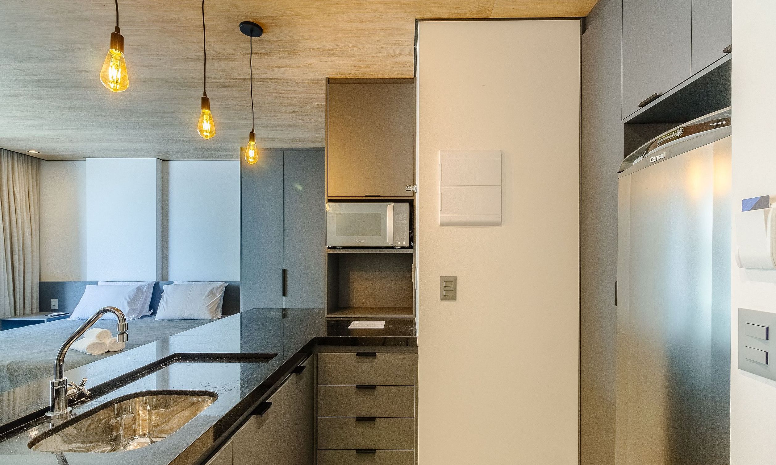 Una cocina moderna con microondas integrado, refrigerador de acero inoxidable y una encimera con lavamanos.