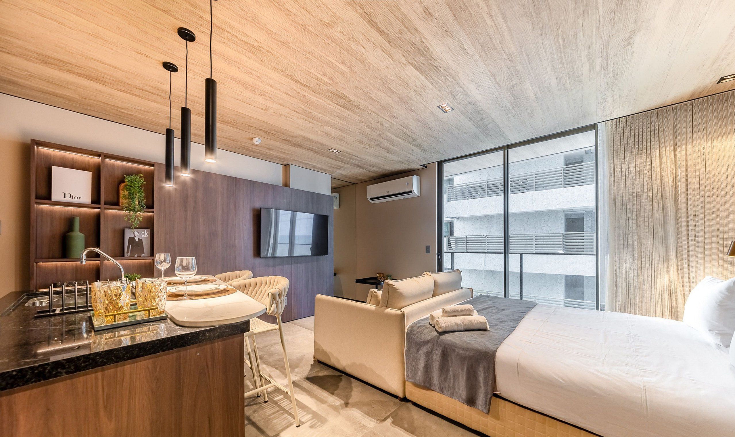 A modern hotel room with a kitchen area, a large bed, and a TV.
