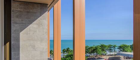 A balcony with a view of the ocean and a beach area with palm trees and beach umbrellas.