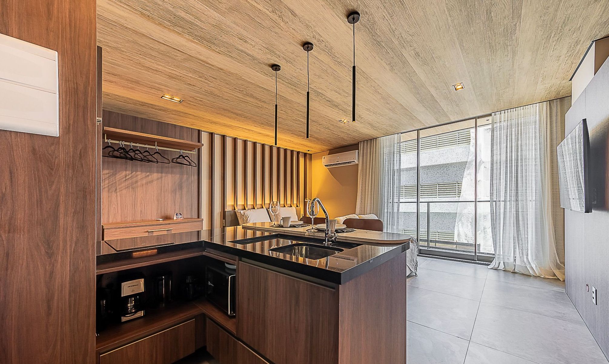 Cocina moderna con una isla central, muebles de madera, iluminación colgante y vistas al exterior.