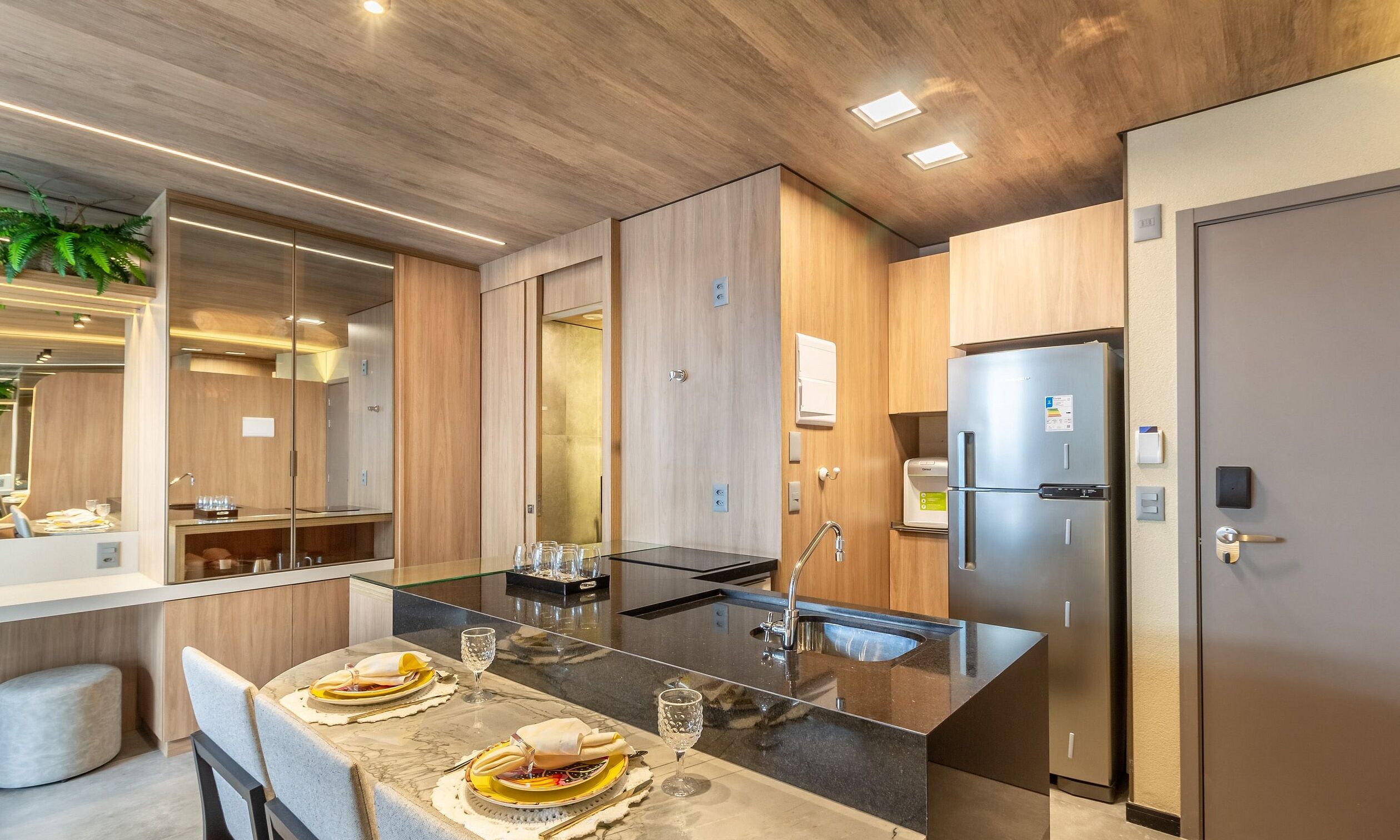Una cocina moderna con una isla central, electrodomésticos de acero inoxidable y un comedor con una mesa dispuesta para dos.