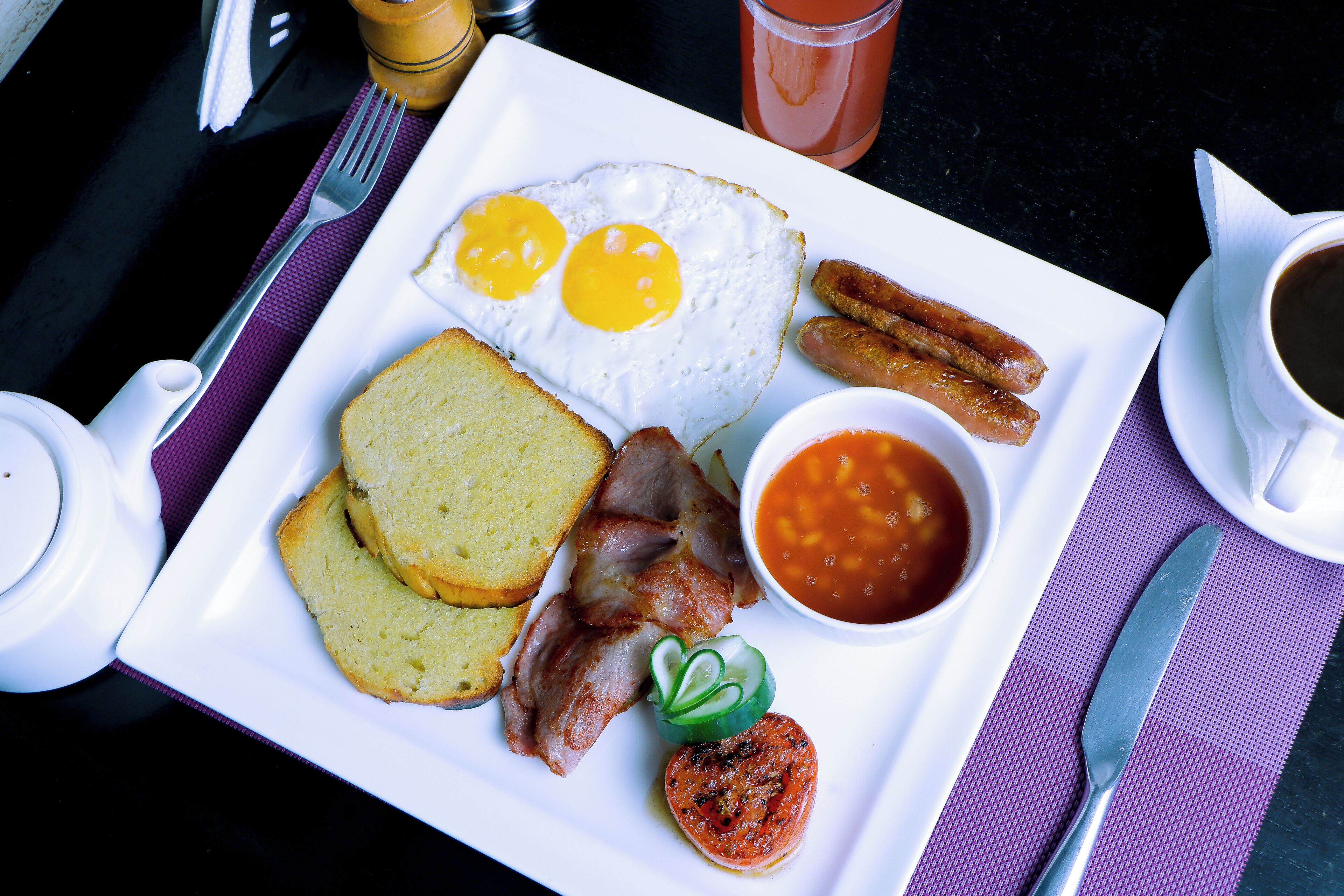 Un plato de desayuno con huevos, salchichas, tocino, tostadas, frijoles y una ensalada pequeña.