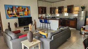 Un salon moderne avec un canapé gris, une petite table sur laquelle est posé un vase, et un tableau abstrait aux couleurs vives accroché au mur.