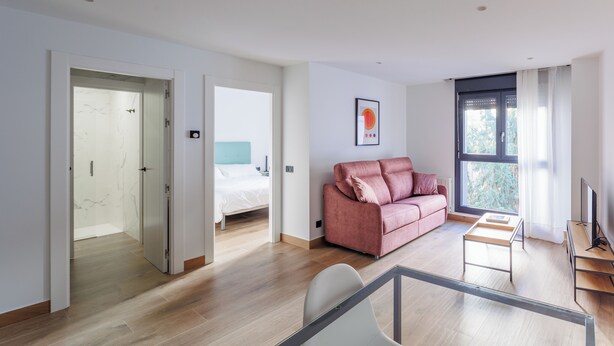 A modern living room with a pink sofa, a TV, and a window with curtains.