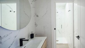 A modern bathroom with a marble wall, a large mirror, a white sink, and a black faucet.