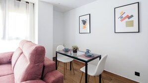 Ett modernt vardagsrum med en rosa soffa, ett glasbord med vita stolar och två inramade konstverk på väggen.