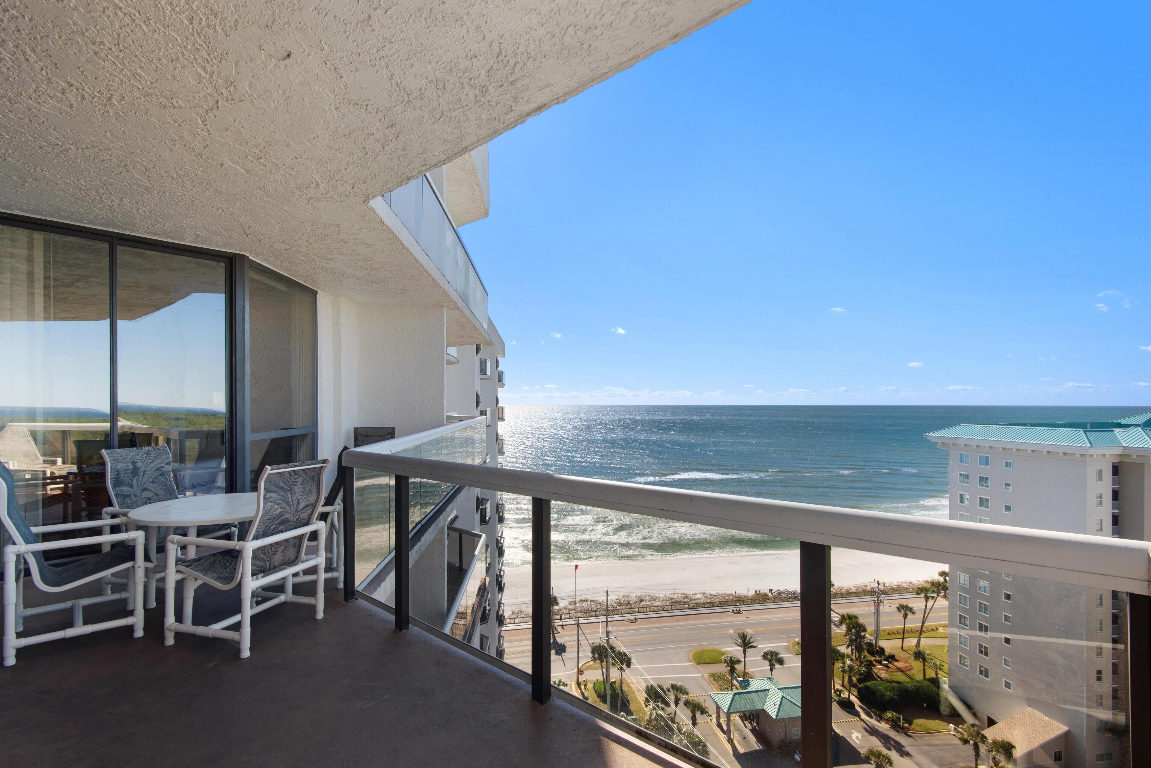 A balcony with a view of the ocean and beach, furnished with white chairs and a table.