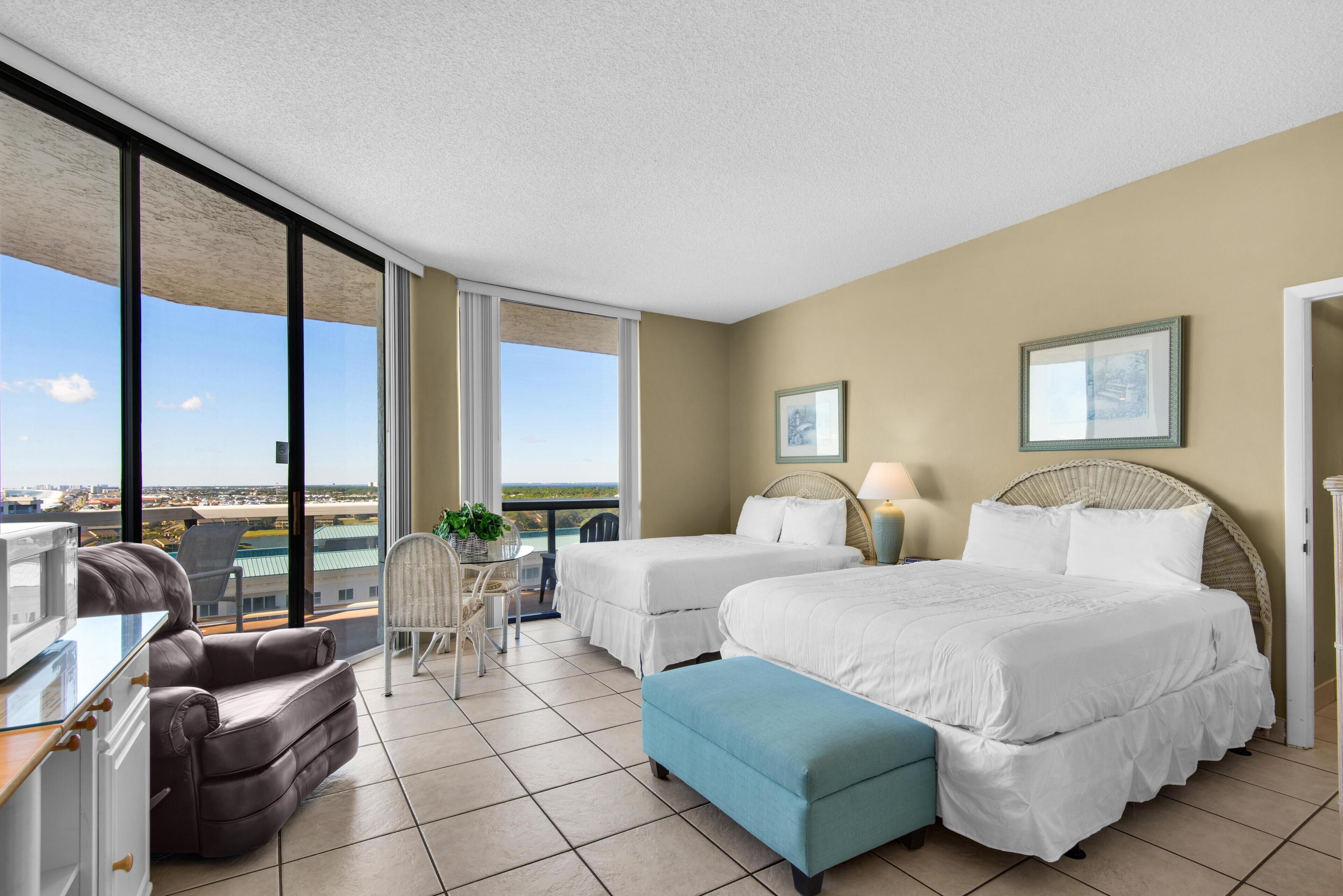 A hotel room with two beds, a sofa, a balcony with a view, and a dining area.