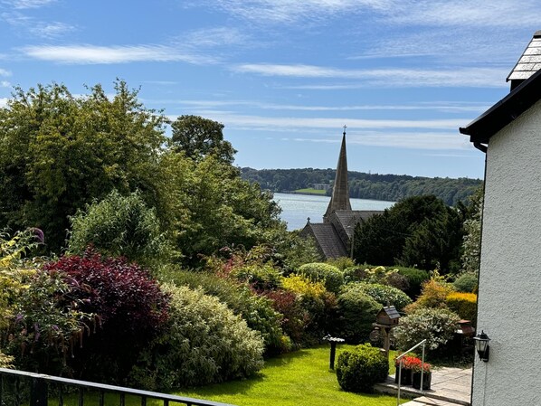 A garden with a variety of plants and a view of a church steeple across a body of water. - Converted Former Rectory - Snowdonia View (Llanfairpwllgwyngyll)