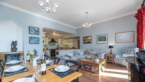 Een ruime woonkamer met een eettafel voor vier personen, een bank, een salontafel en een keuken op de achtergrond.
