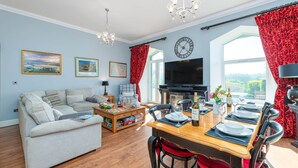 Een woonkamer met een bank, een eettafel voor vier personen, een televisie en een open haard.