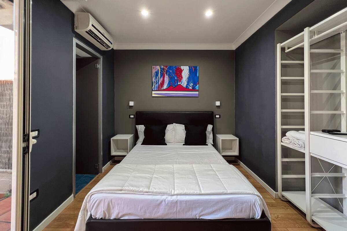 A modern bedroom with a large bed, a bedside table, a wardrobe, and a painting on the wall.