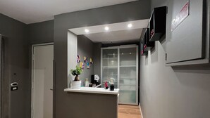 A reception area with a reception desk, a potted plant, a wall-mounted TV, and a glass door leading to a room. - Tiè tiè (Naples)