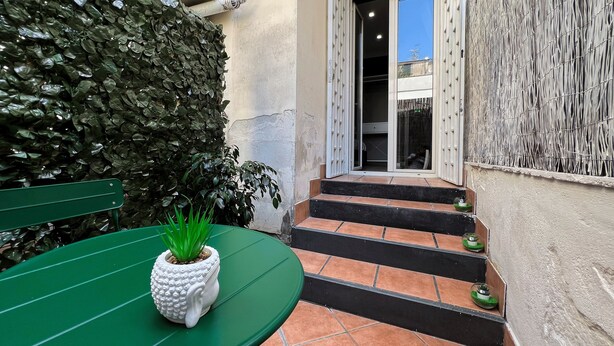 A courtyard with a green table, steps leading to a door, and a wall with a textured pattern. - Tiè tiè (Naples)