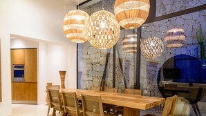 A modern dining area with a wooden table and chairs, stone wall, and hanging woven light fixtures. - Modern Villa in Santa Eulalia (Santa Eulalia del Rio)