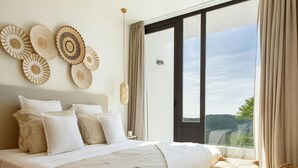A spacious bedroom with a large bed, a bench, and a view of the outdoors. - Modern Villa in Santa Eulalia (Santa Eulalia del Rio)