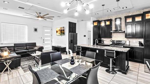 A modern kitchen with dark cabinetry, a central island, and a dining area with a glass table and chairs.