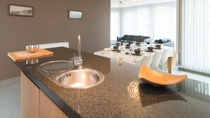 A modern kitchen with a granite countertop, stainless steel sink, and a dining area with a table set for four. - Penthouse in Ostend With sea View Dining (Ostend)
