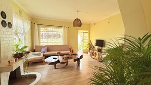 Un salon spacieux avec un canapé, une table basse et une cheminée. On y trouve également des plantes en pot et un téléviseur posé sur un meuble.