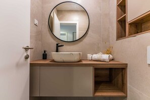 A modern bathroom with a round mirror, a white basin, a black faucet, and a wooden vanity. - Apartment Leonarda (Zadar)