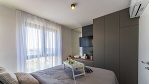 A modern bedroom with a bed, a bedside table with a lamp, a TV mounted on the wall, and a window with sheer curtains. - Apartment Leonarda (Zadar)