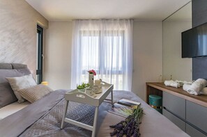 A modern hotel room with a bed, a bedside table with a vase of flowers, a small table with a magazine, and a TV mounted on the wall. - Apartment Leonarda (Zadar)