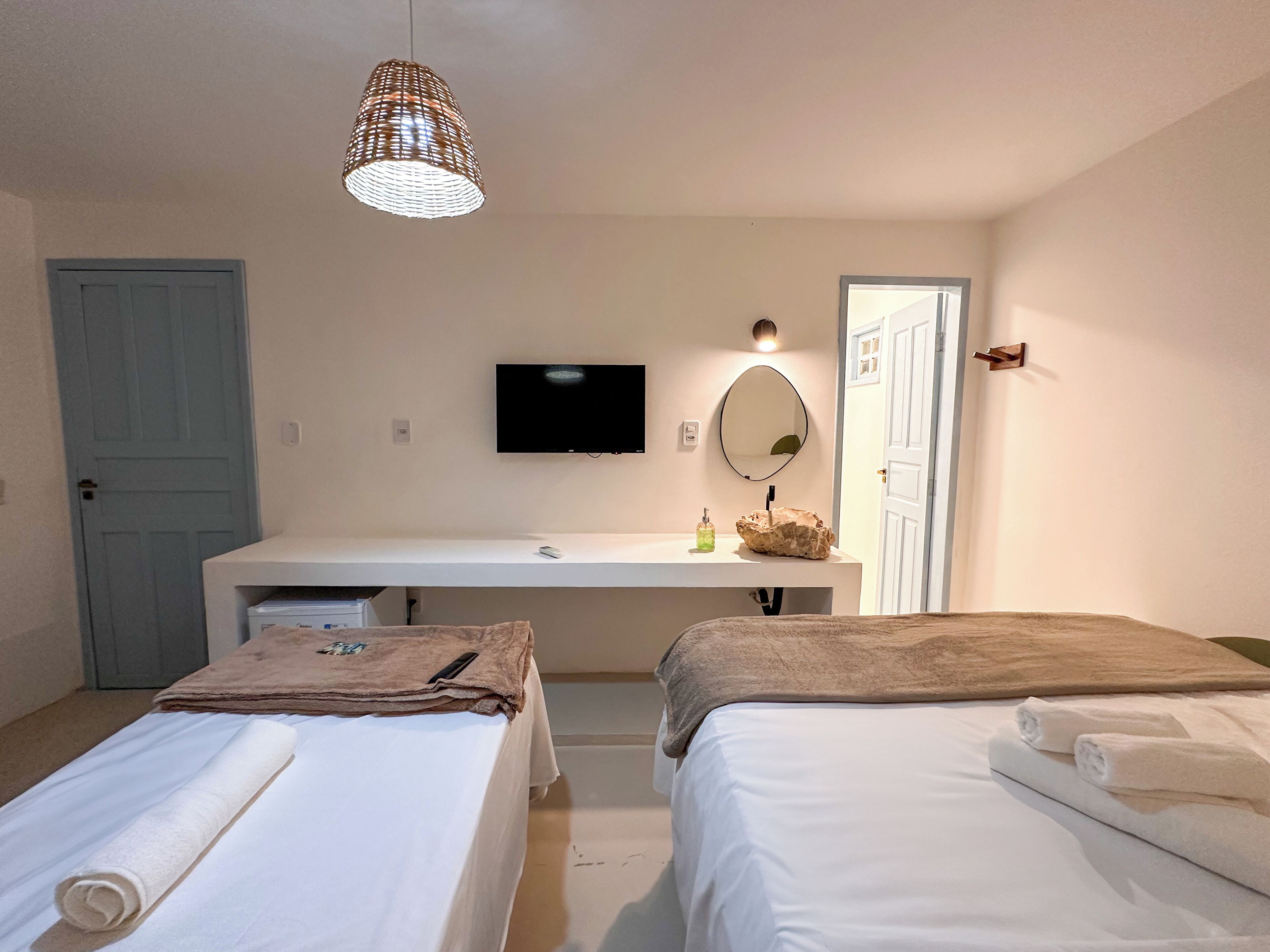 A hotel room with a bed, a bedside table, a TV, a mirror, and a hanging light fixture.