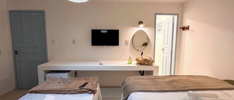 A hotel room with a bed, a bedside table, a TV, a mirror, and a hanging light fixture.