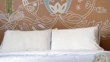 A bed with white bedding and a pillow, set against a wall with a floral and abstract mural.