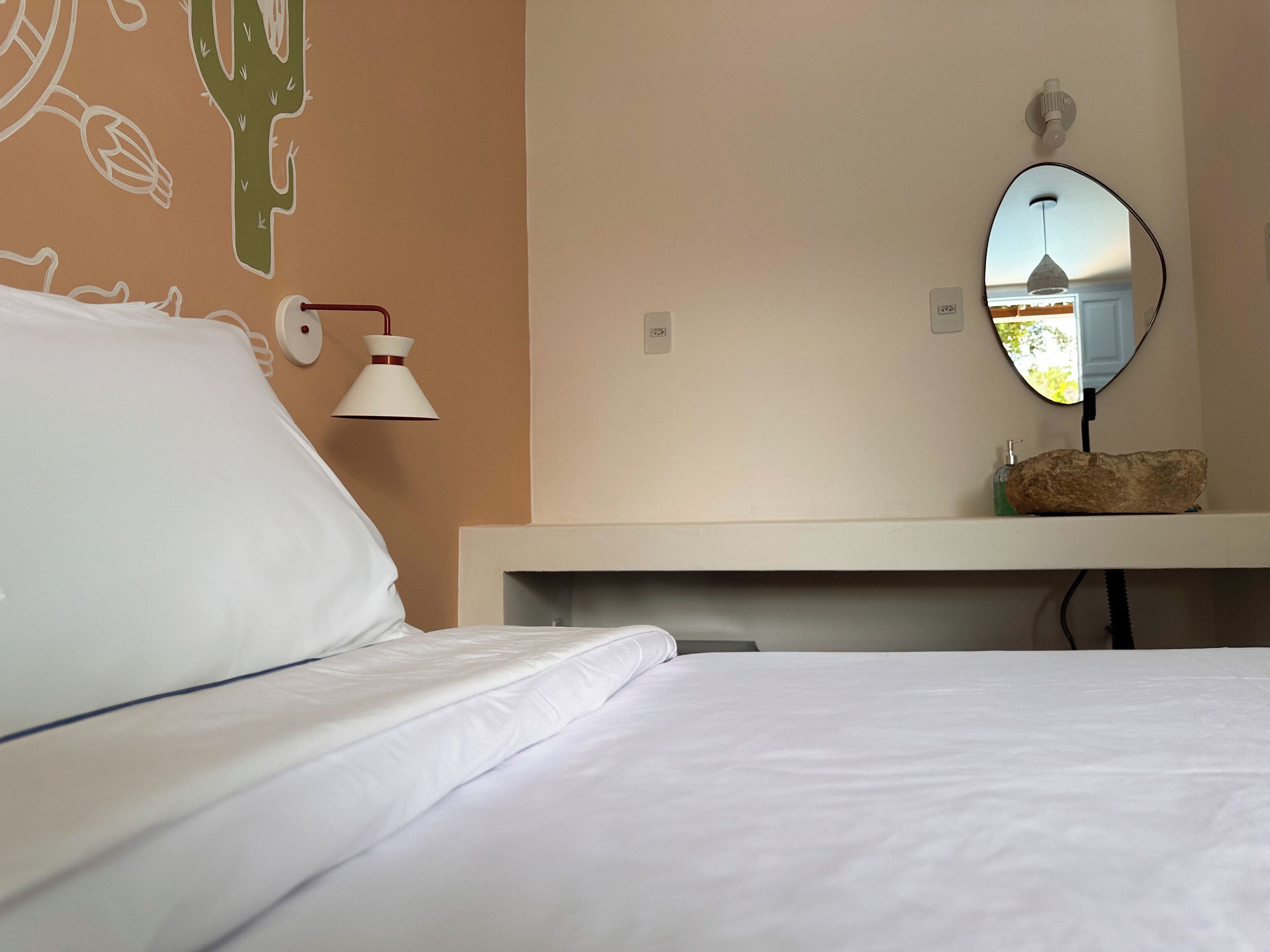 Habitación de hotel con cama, espejo en la pared, lámpara de noche y decoración de cactus.