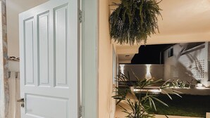 An open door leading to a well-lit outdoor area with a potted plant and a hanging fern. - Vilab  (Porto Seguro)