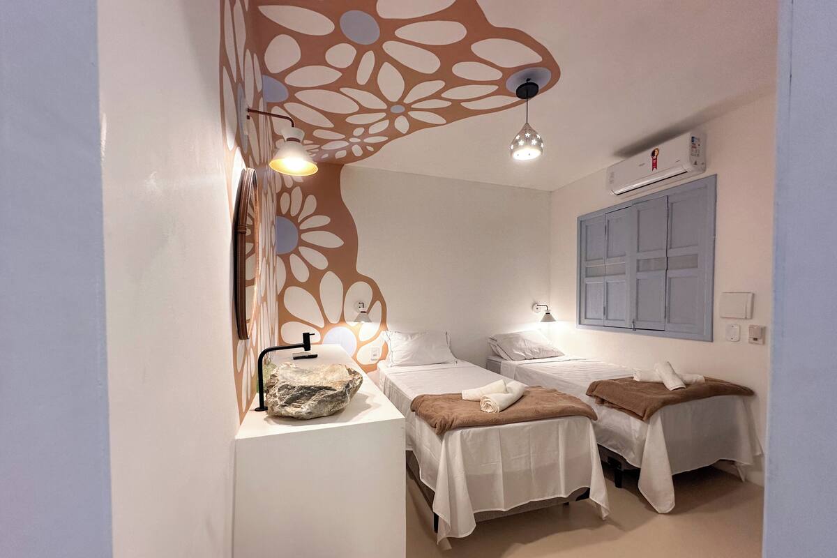 Une chambre avec deux lits, un mur décoratif, un lavabo et une fenêtre avec des volets.