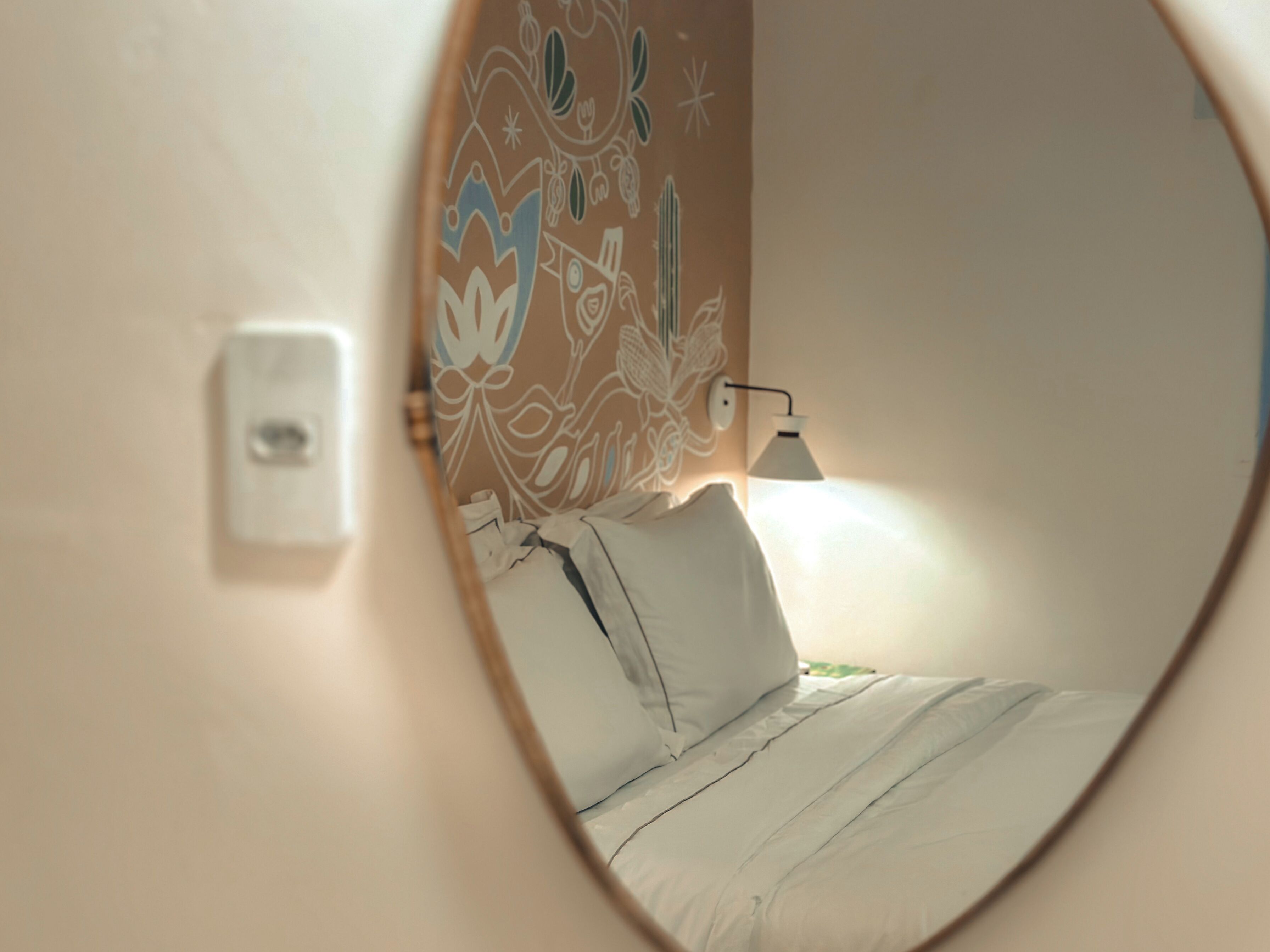 A circular window view of a bedroom with a bed, a wall-mounted light, and a power outlet.