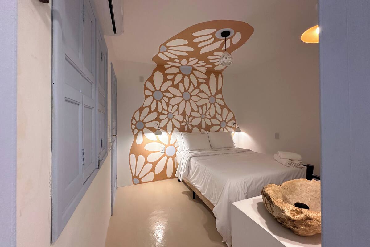 Une chambre à coucher comprenant un lit, un climatiseur fixé au mur, un panneau décoratif mural, une table de chevet et une lampe.