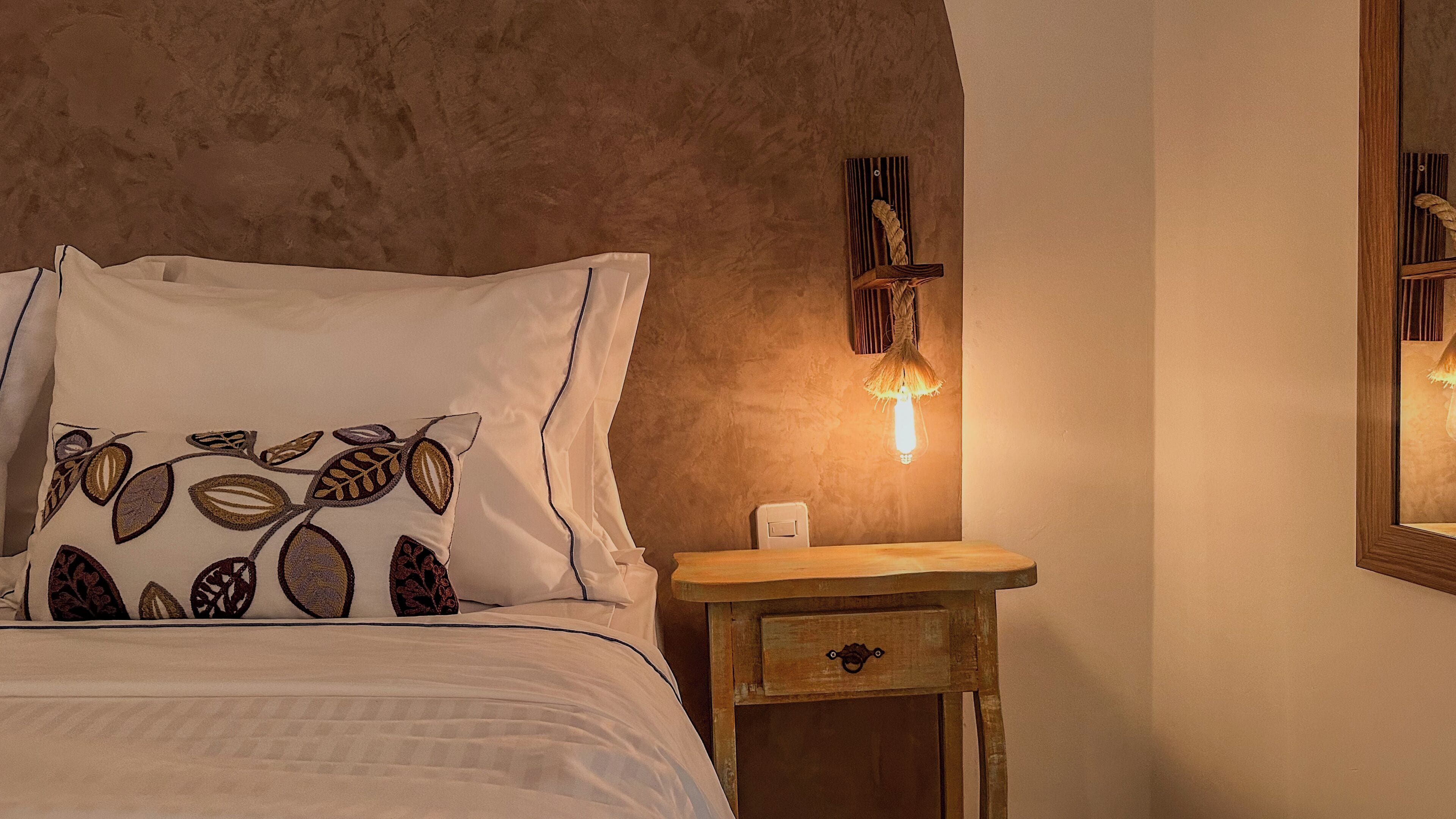 A bedroom with a bed, a nightstand, a wall-mounted lamp, and a framed picture.
