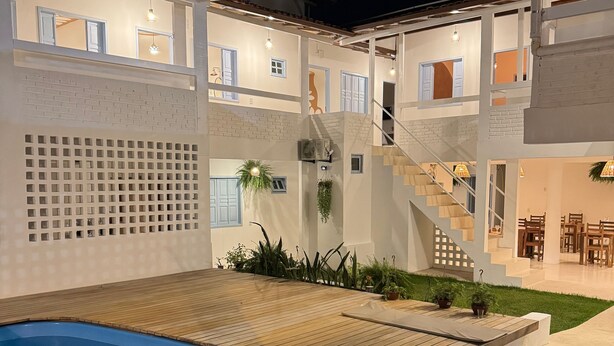 A modern outdoor pool area with a wooden deck, a staircase, and a dining area with chairs and tables. - Vilab  (Porto Seguro)