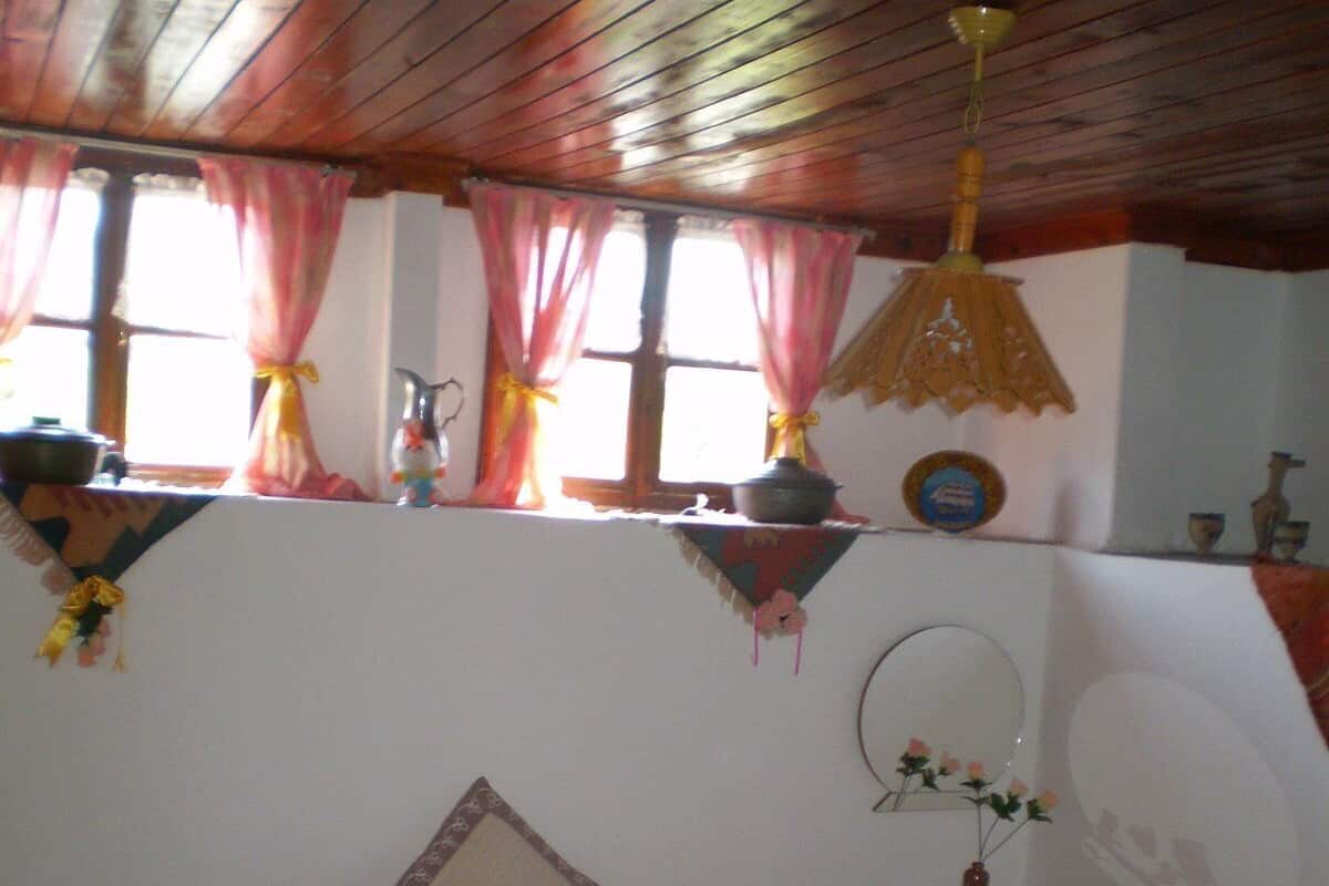 Ein Schlafzimmer mit Holzboden, einem Bett mit rosa und weißer Bettwäsche, einem Nachttisch mit Spiegel und einem Fenster mit Vorhängen.