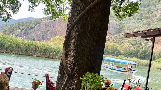 A table with dessert plates, a glass of juice, and a cup of coffee, set outdoors with a view of a river and boats. - Vome (Ortaca)