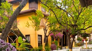 A courtyard with a yellow building, potted plants, and a tiled walkway. - Vome (Ortaca)