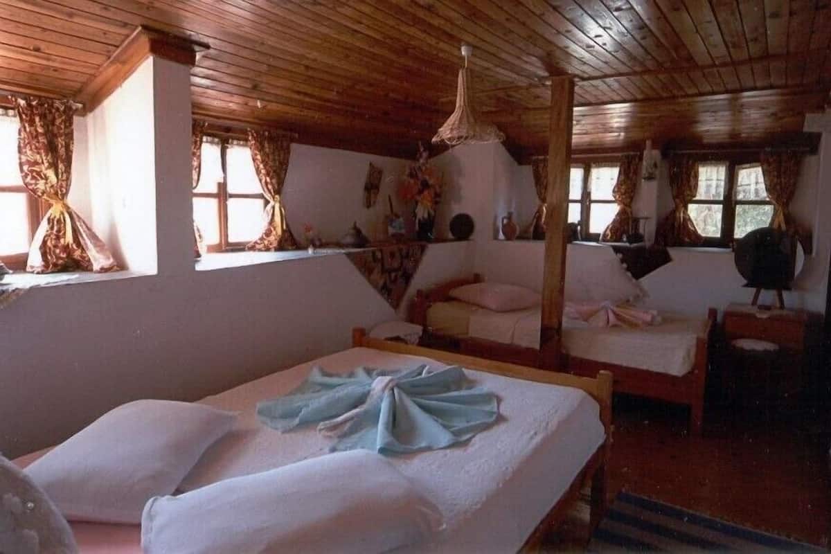 Eine rustikale Holzhütte mit Holzbalkendecken und -wänden, zwei Betten mit weißen Leinen und einem großen Fenster mit Vorhängen.