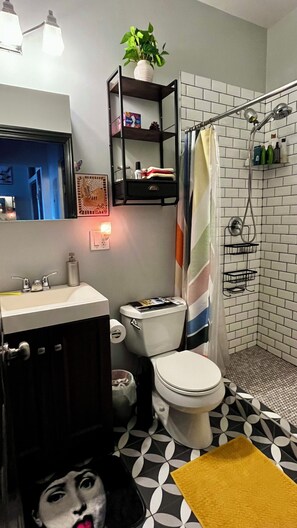 A bathroom with a toilet, sink, and shower. There is a shelf above the toilet and a plant on it. - Cozy & Chic 2BR Loft on 18th St in Chicago (Chicago)