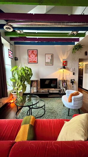 A modern living room with a red sofa, a glass coffee table, a large potted plant, a flat-screen TV, and a bookshelf. - Cozy & Chic 2BR Loft on 18th St in Chicago (Chicago)